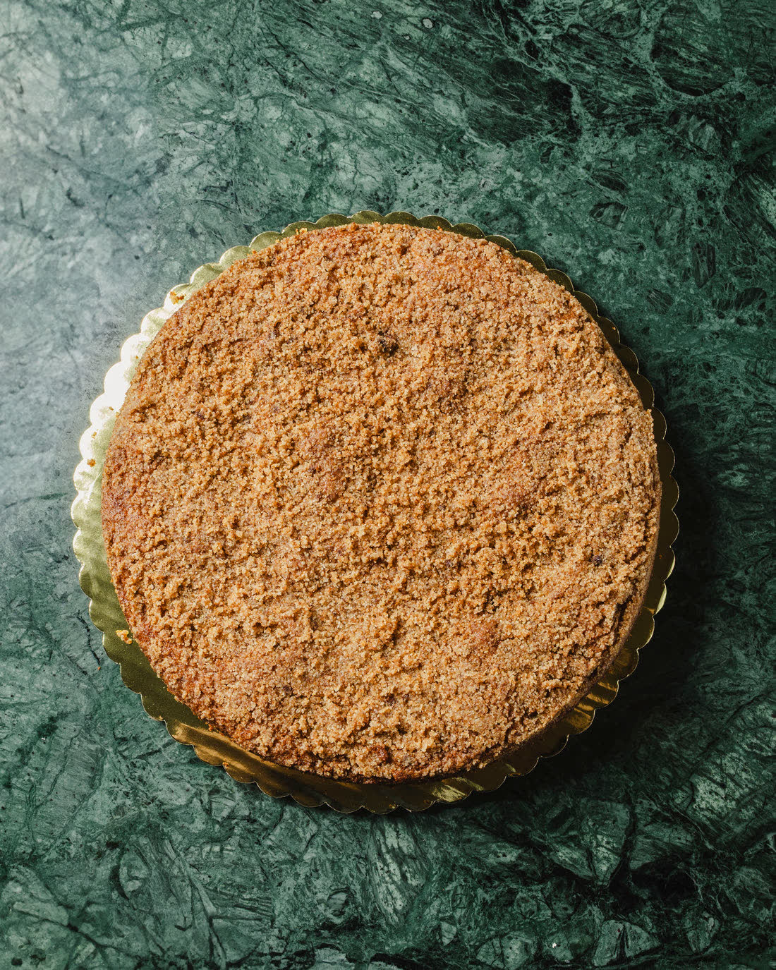 Cinnamon Coffee Cake entero cubierto de streusel, cenital sobre su tarima dorada en mármol verde