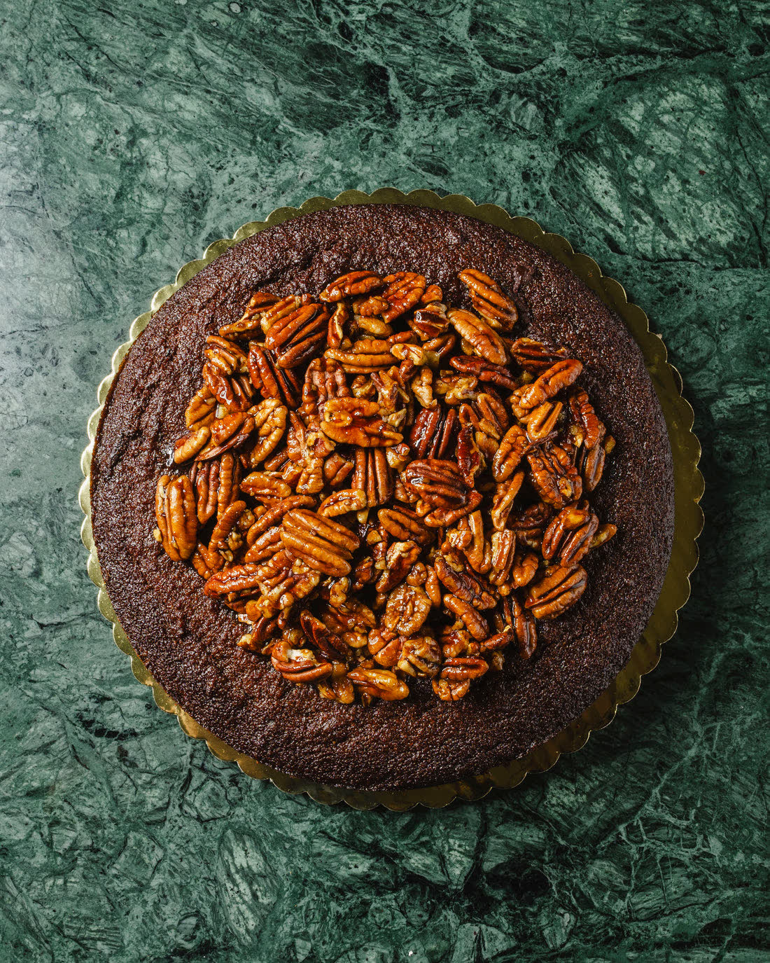 Sticky Date Cake entero coronado de pecans, cenital sobre su tarima dorada en mármol verde